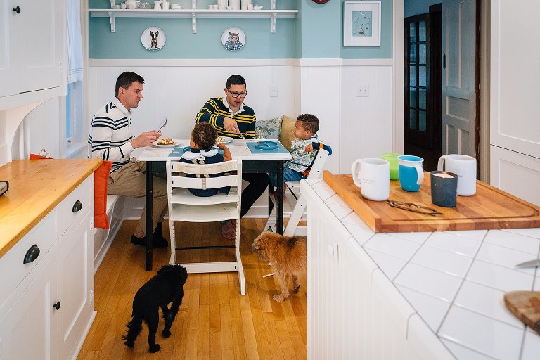 Family of two dads, two kids, and two dogs are in the kitchen, having breakfast together. 