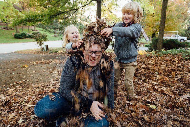 motion filled image of two children dumping leaves on their dad during an autumn at home session