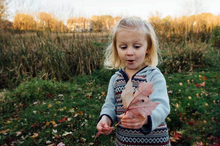 girl in autumn dress is surprised by large colorful leaf