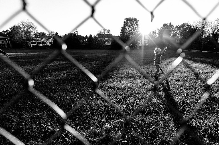 image taken through the fence of a boy holding baseball and bat. Fence is diamond pattern. 
