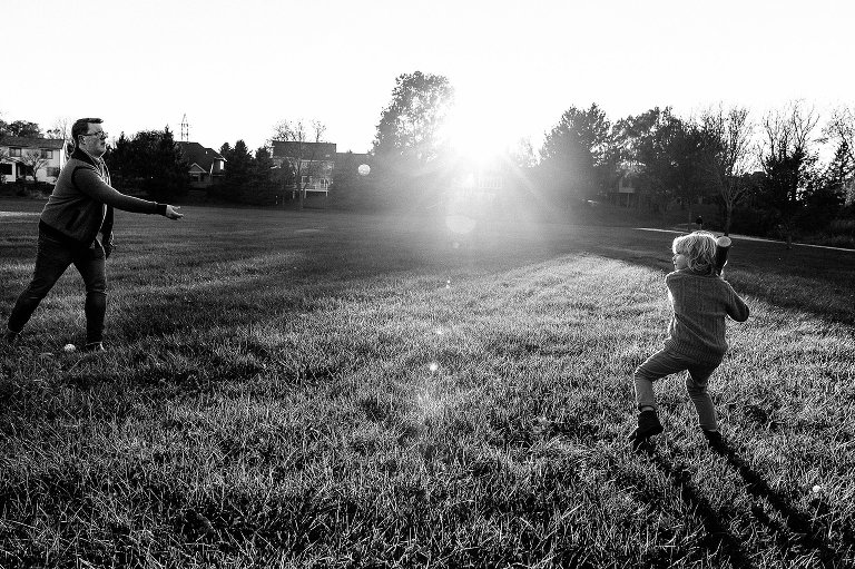dad pitches baseball to young son with a bat with setting sun between them