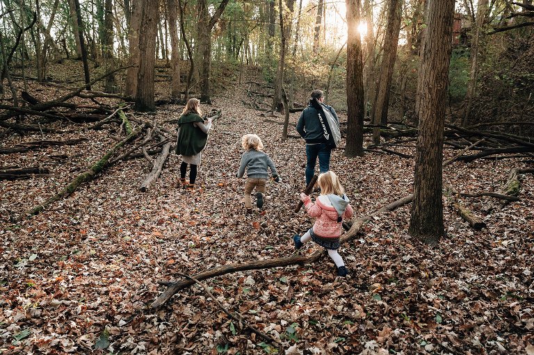 family of four hike through a forest filled with leaves and setting sun