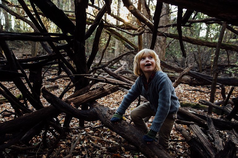 boy looks up from inside a tree fort. Smiling. Light hits face. 