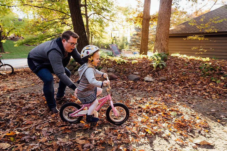 dad pushes daughter on bike during autumn night at home 