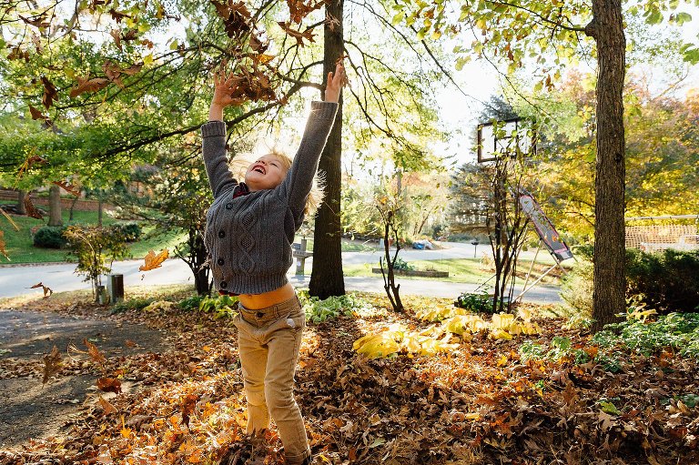 boy throws up leaves in a Autumn at Home session