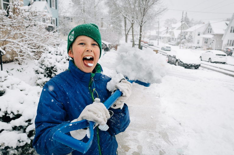 Boy stands in snowstorm holding a shovel of snow