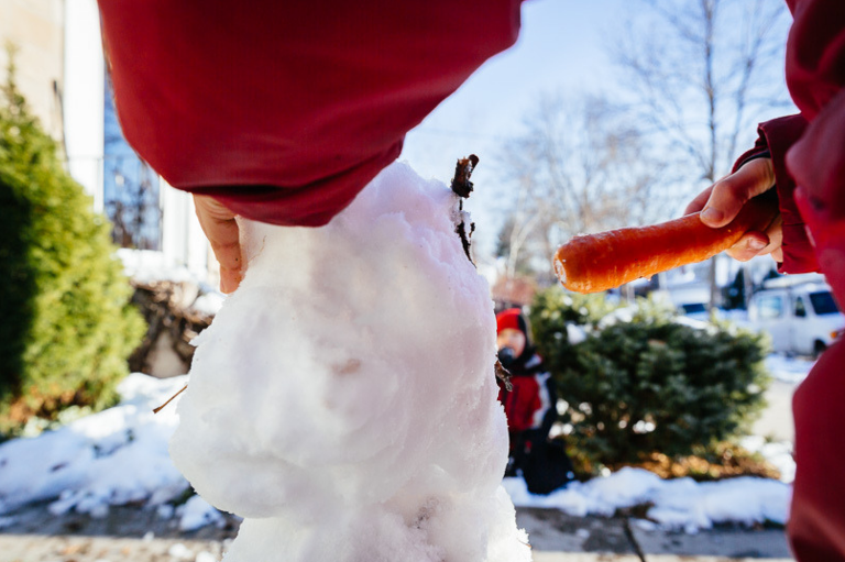 Snowman with a child's hand putting an orange carrot nose in the center 