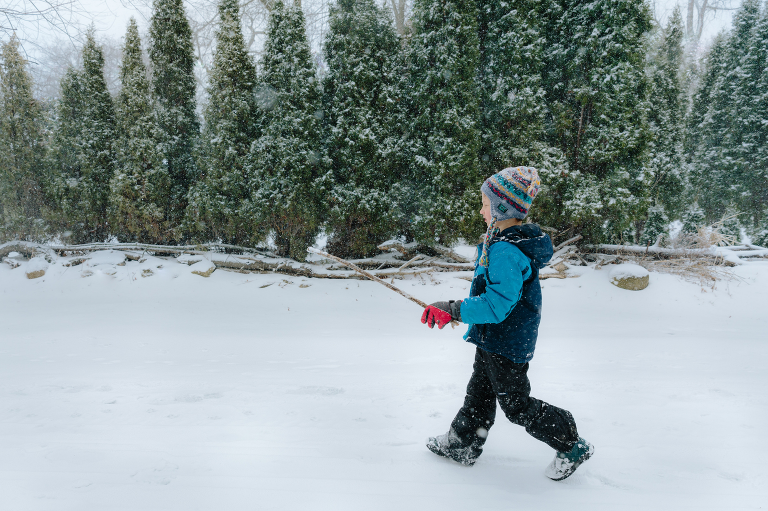 Boy walks through snowy scene holding a stick