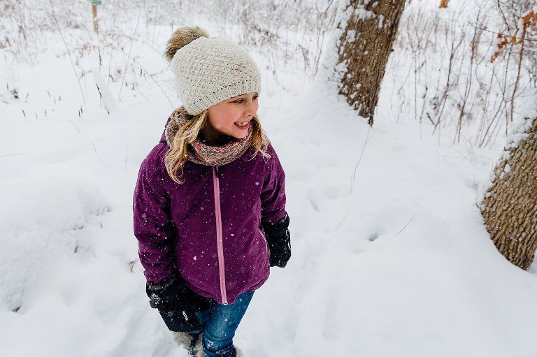 young girl looks to the right and smiles while standing in knee-high snow. madison family photographer 