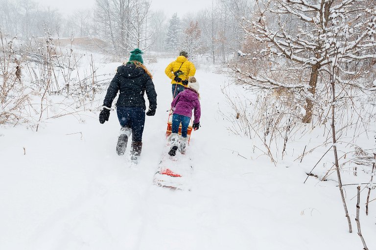Family of three runs in the snow while pulling a red sled. madison family photographer 