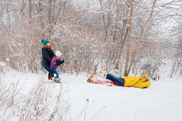 Mom and daughter pull dad on a sled in the middle of a snowstorm.  madison family photographer 