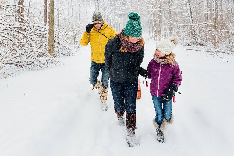 Mom, Dad, and young Daughter walk in snowy forest and chat together.  Madison WI photographer