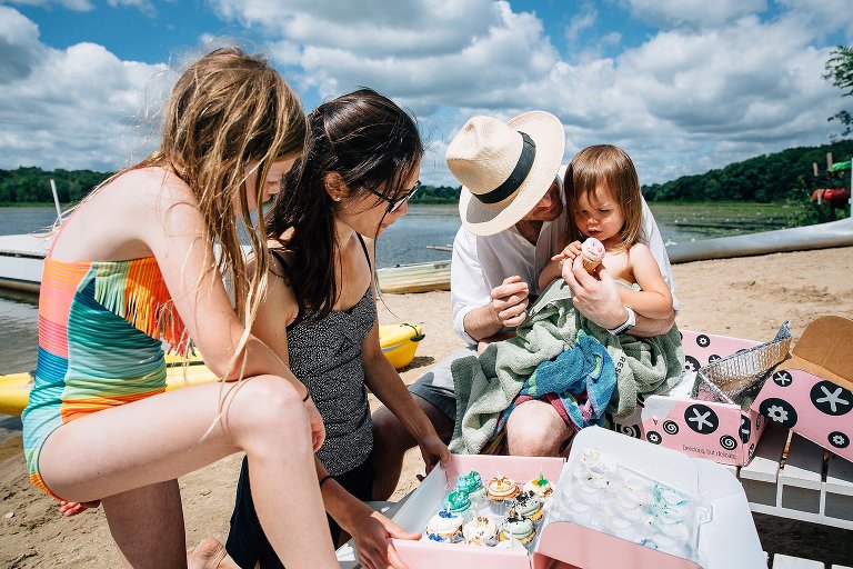 2yo starts to unwrap cupcake liner while other family members look at the cupcakes in the box. At the beach. 