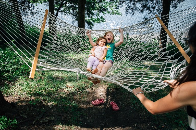 Two girls laugh while their mom pushes/pulls them on a big hammock. 