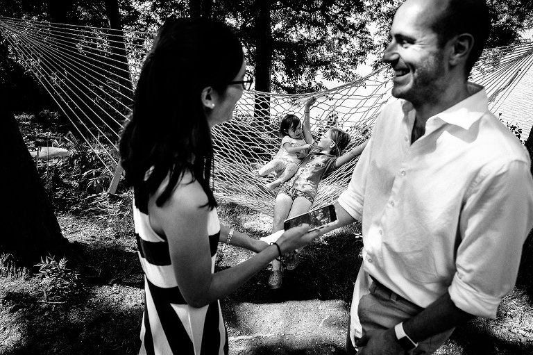 Framed by out of focus parents laughing, girls silly on hammock in focus in background 