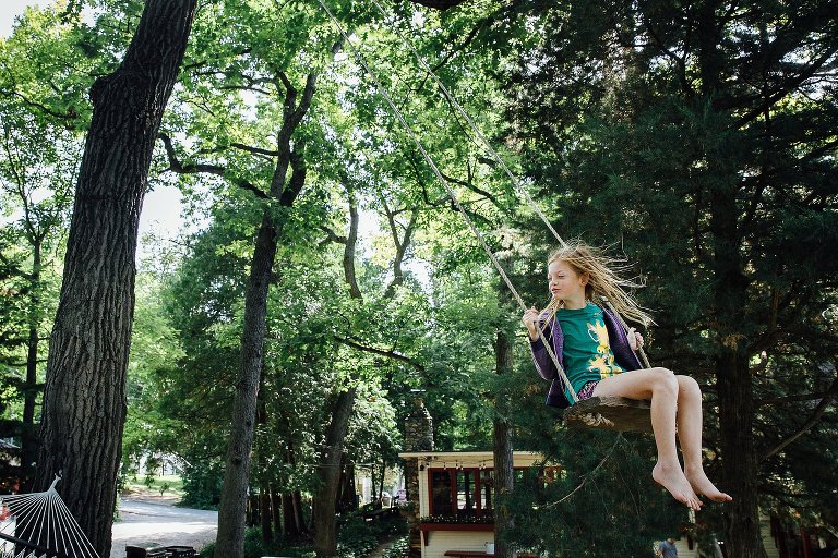 young girl swings on a bench swing in a tall tree. wind in her hair. 