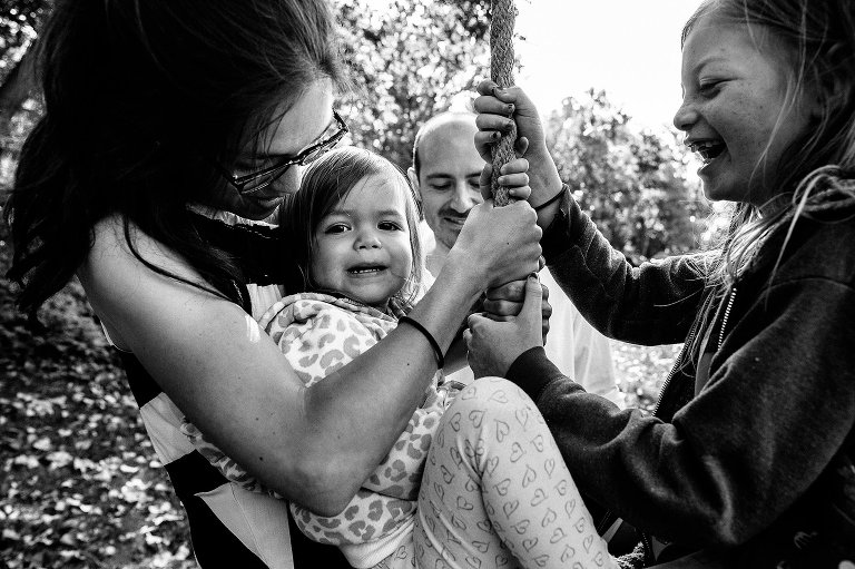 black and white. Mom, two daughters share a tire swing ride--dad pushes. 