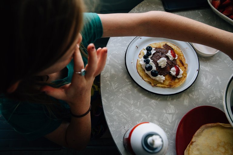Chlid makes a silly face on her crepe with whipped cream and fruit for eyes nose and mouth. 