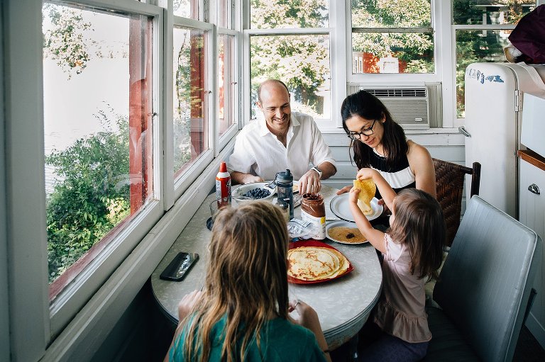 Family of 4 sitting down to breakfast crepes in a small cabin. 