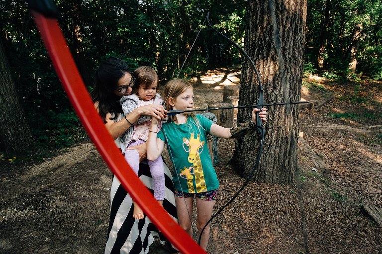 Mom and two daughters hold bow and arrow together for archery practice