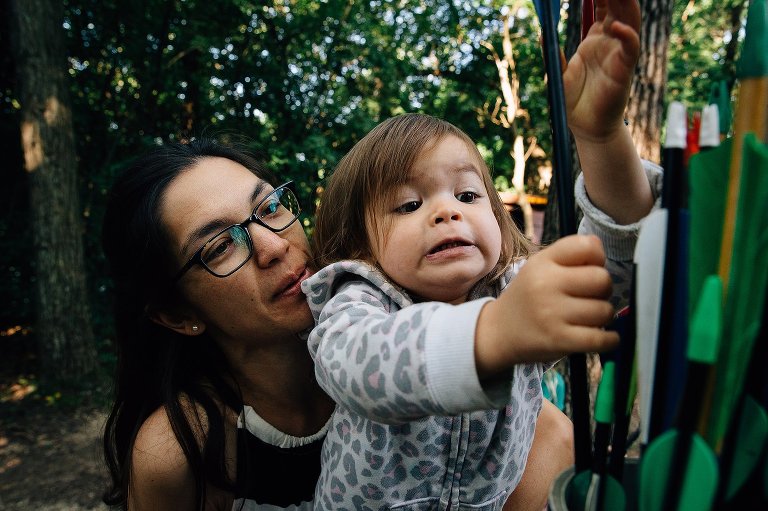 2 year old make a concentration face as she tried to pull arrows out of the holder. Her mother is holding her, smiling. 