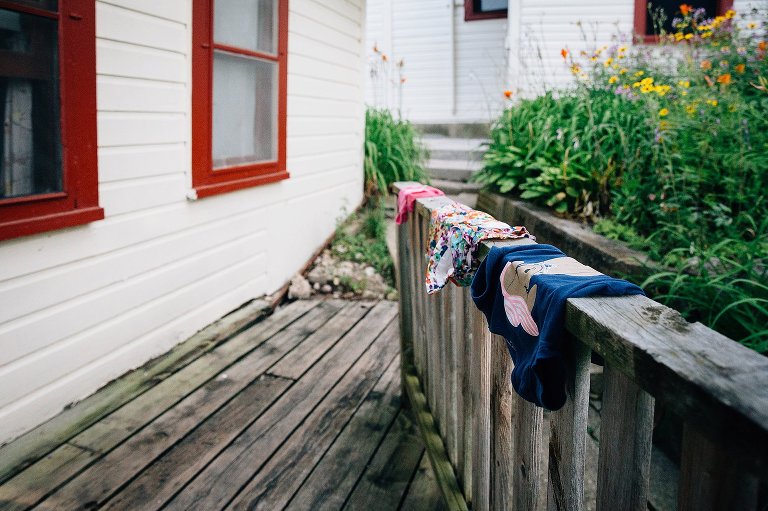 Swimsuits lay drying over deck railing. Summer flowers bloom in the background. 