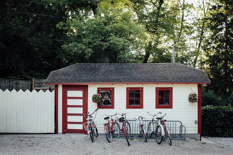 Early morning sun rises above big green oak trees, a red shed and six old-fashioned bicycles. 