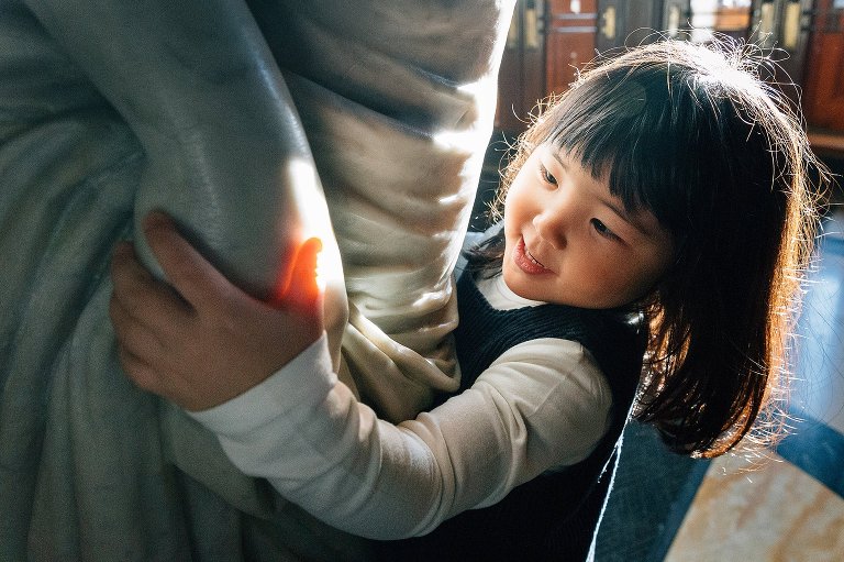 4yo girl plays with a statue in bright light.  She smiles. 