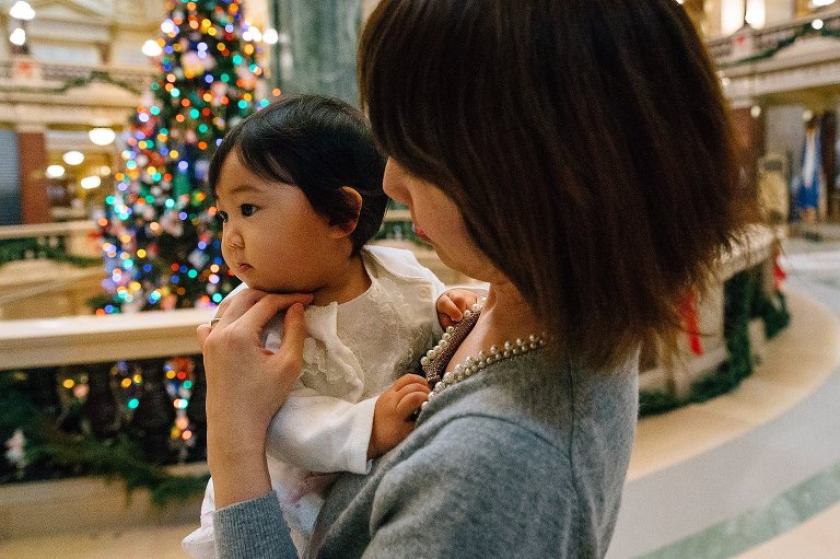 Mother gently holds daughter and places hand under her chin. Large Christmas tree in the background. 