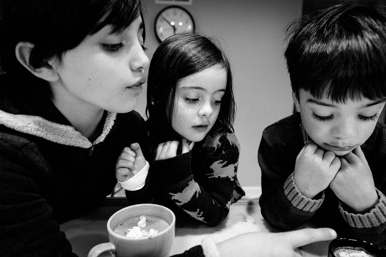 black and white. 3 kids look at hot chocolate at home. 