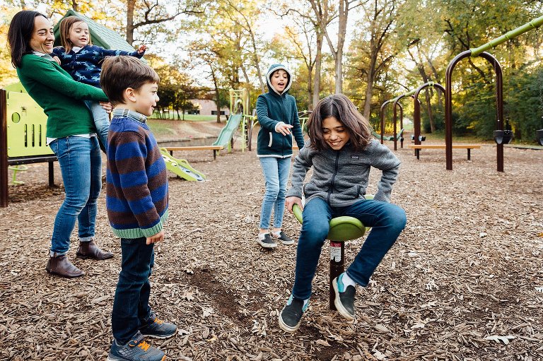 Teen boy spins on playground equipment while siblings watch. 