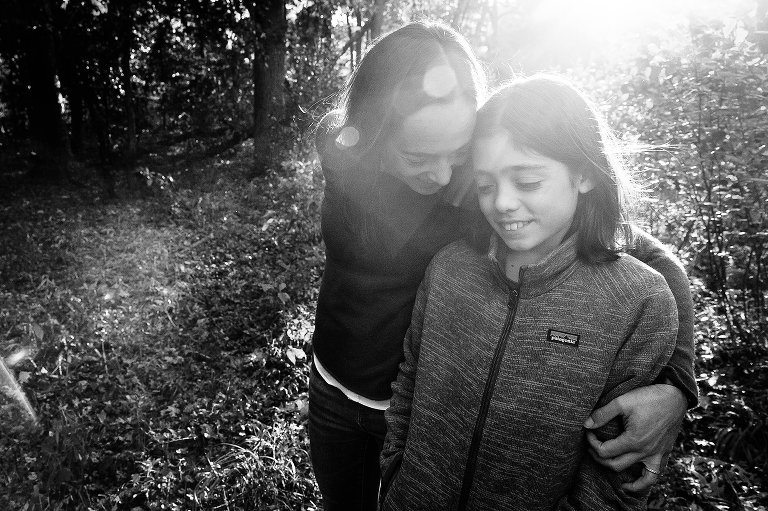 Black and white. Mom hugs teen boy. Sun flare present. 