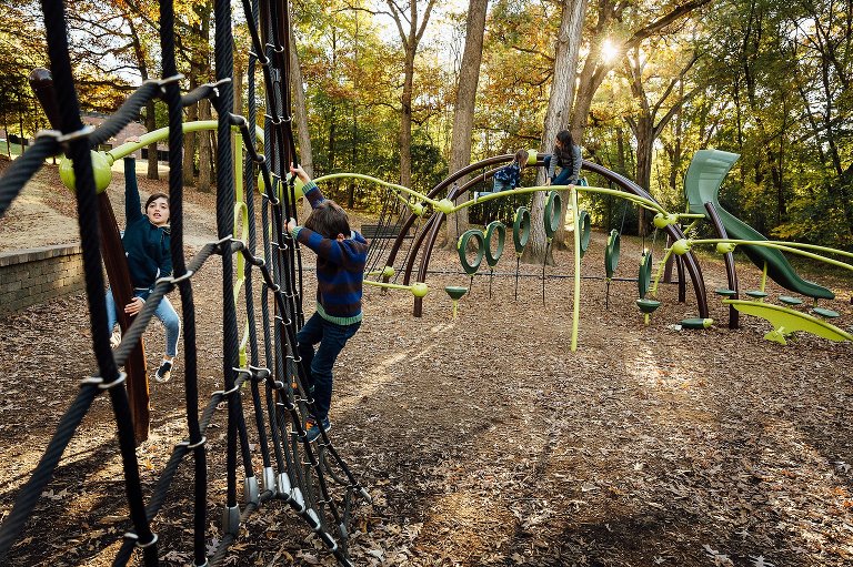 Two kids play on playground equipment in foreground, while 2 kids play on playground equipment in background. 