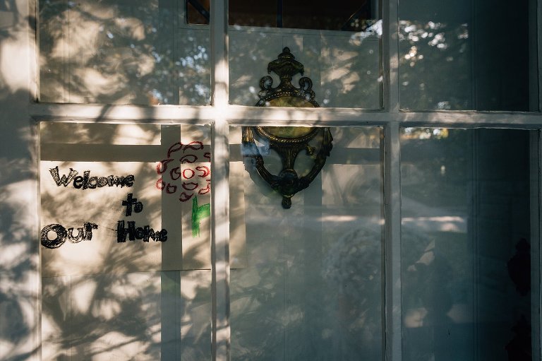 Dappled sunlight hits the from door where a child has made a "welcome to hour home" sign and taped it. 