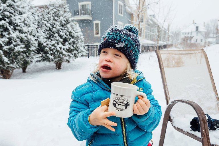 Preschool girl holds a cup of hot chocolate and a graham cracker. 