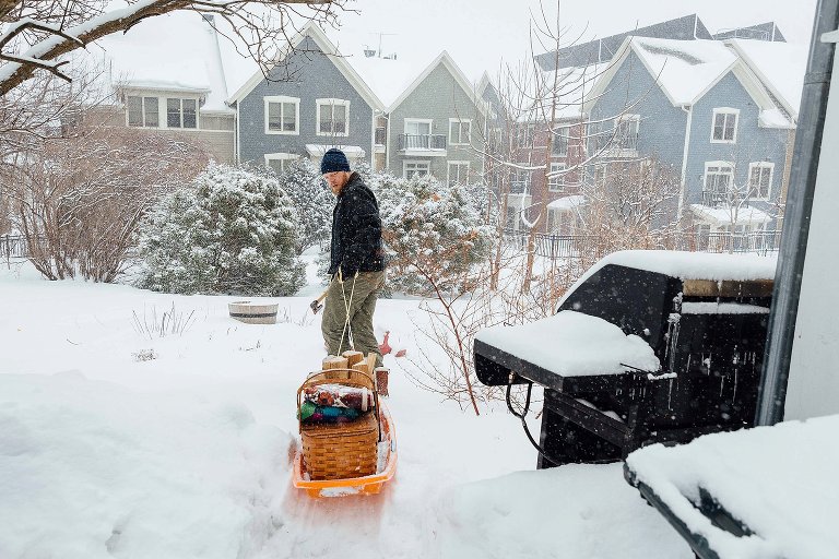 Dad uses the sled to carry campfire supplies to the backyard in a snowstorm. 