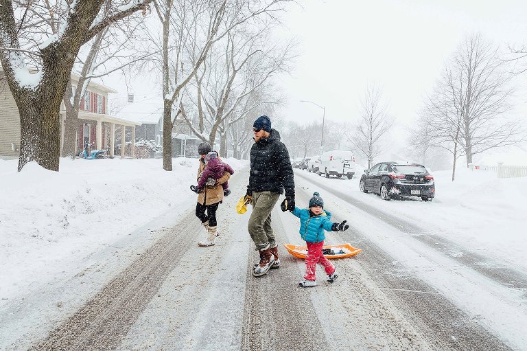 Family crossed a busy street in the middle of a snowstorm. 