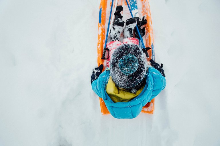 Top view of snowy hat while girl rides in an orange sled.
