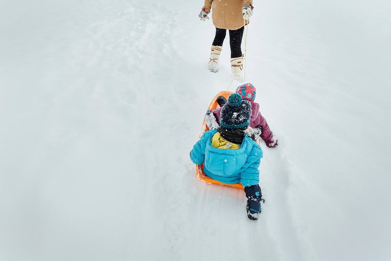 Girls drag their hands in the snow to while being pulled in a sled.