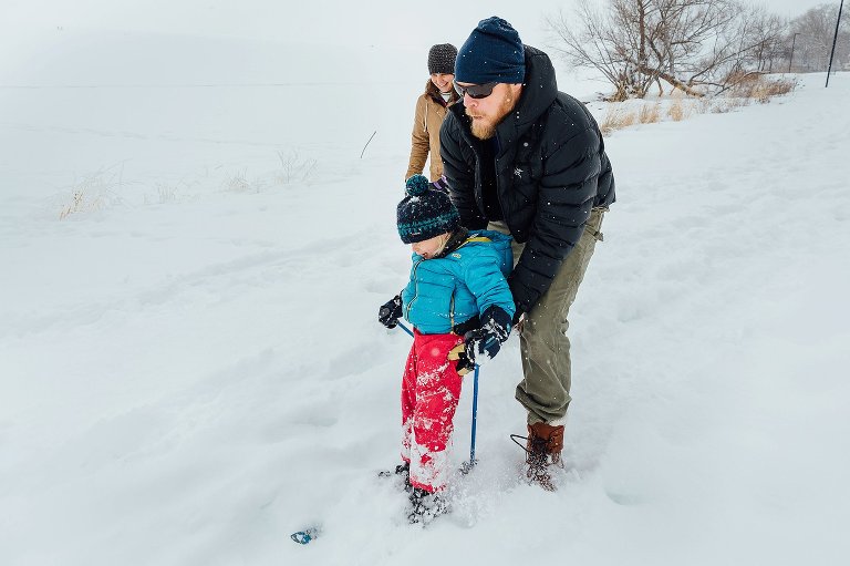 Dad helps daughter go faster on her skis. Everyone smiling.