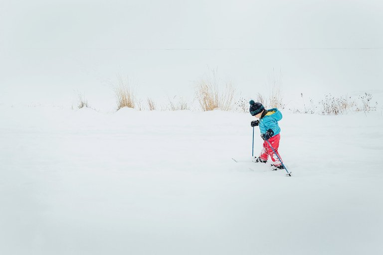 Daughter skis by herself on a path next to frozen lake.
