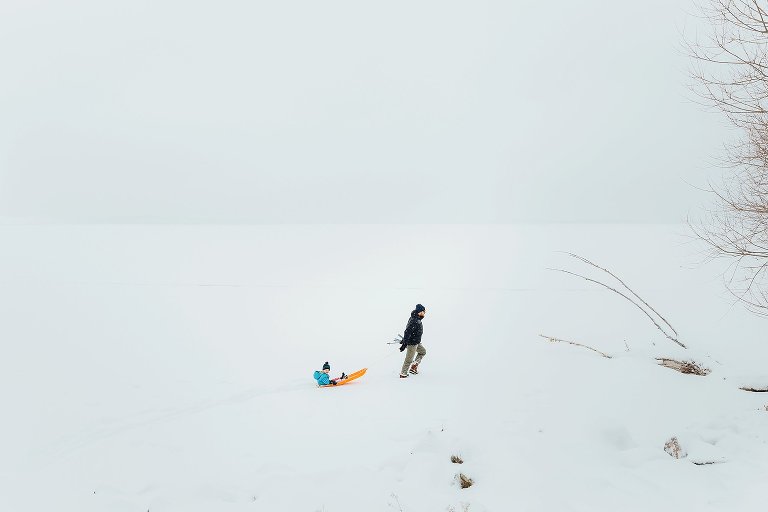 Dad pulls daughter on a sled in middle of frozen lake in a snowstorm. White out conditions.