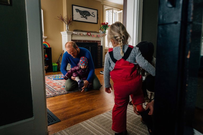 Dad helps young daughter while mom helps older daughter put on winter snow gear.