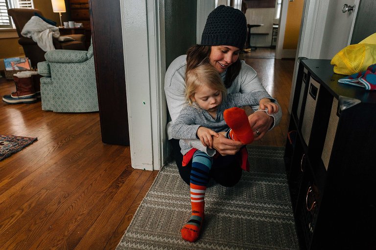 mother helps her daughter put on striped socks in their hallway