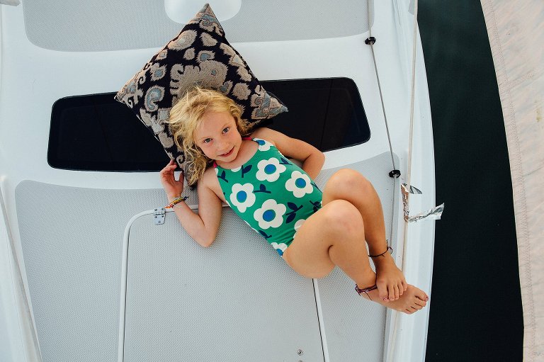 Top down view of girl on the bow of the sailboat. She is camera aware, laying on a pillow, relaxing.