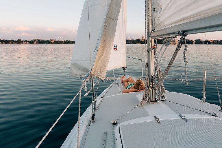Girl lies on bow of the sailboat with sunset reflected on the horizon. madison family photographer