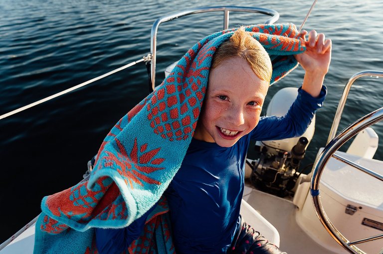 Young boy smiles from behind a towel sailing on Lake Mendota on a Madison family photography session