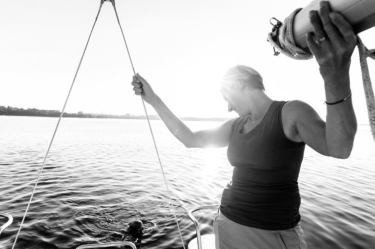 woman holds onto sailboat beam while watching daughter swim back to the boat.