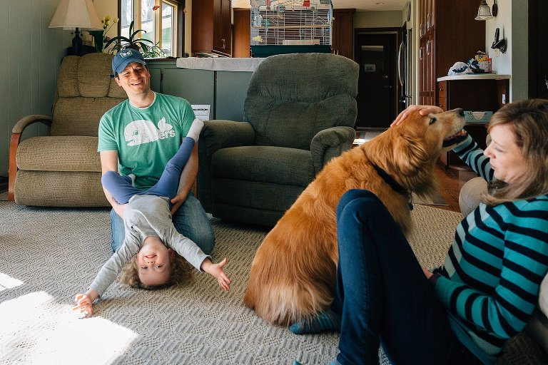 Woman pets Golden Retriever dog while girl plays with dad next to them. 