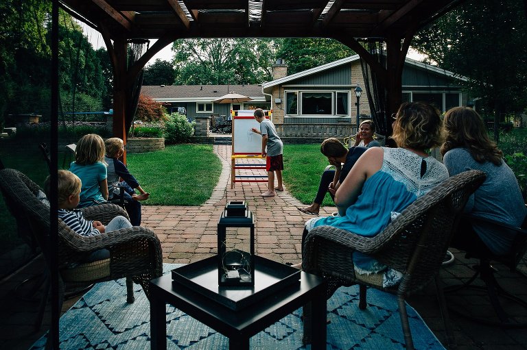 Family gathers in a pavilion to play Pictionary together. Boy at the easel. 